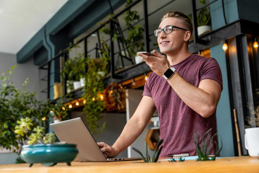 Smart young caucasian business man freelancer it worker guy manager male student recording voice message talking on mobile smart phone with customers partners while working studding in office cafe